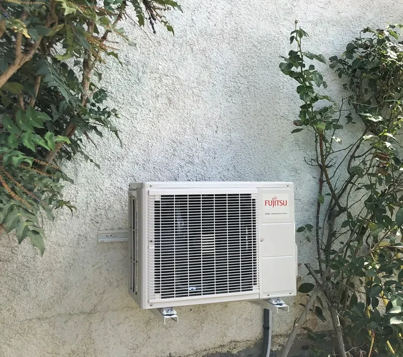 Extérieur résidentiel avec unité de climatisation Fujitsu installée contre mur crépi blanc