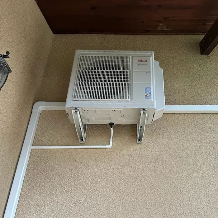 Mur extérieur beige avec unité de climatisation Fujitsu blanche montée sur support mural métallique